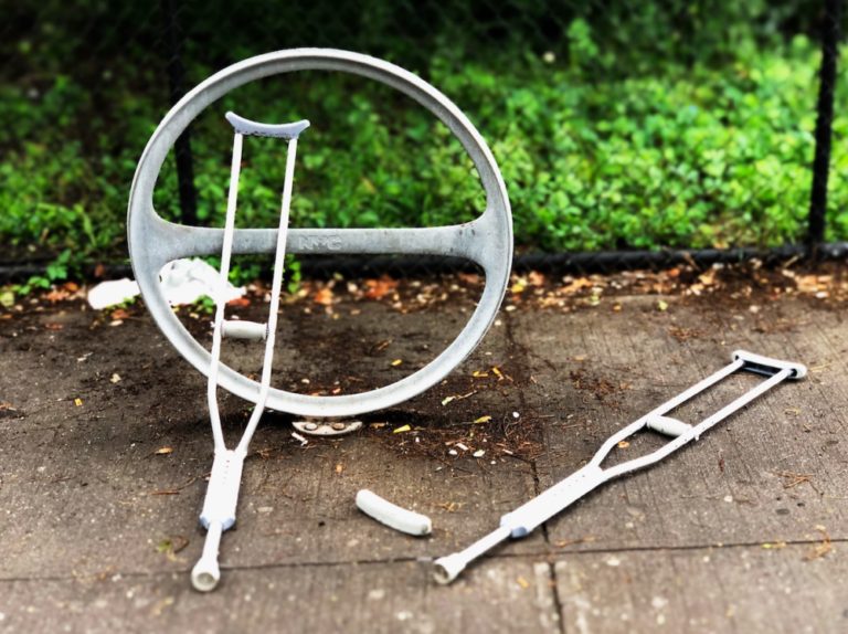 Bent and broken crutches leaning against a circular bike rack on the sidewalk