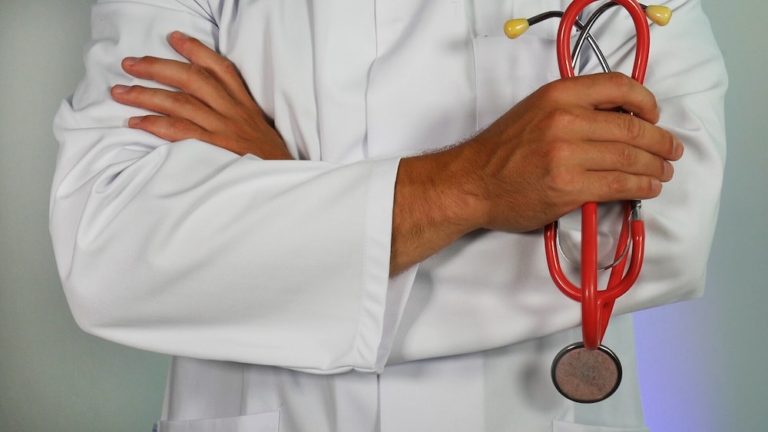 Doctor in white lab coat with arms folded holding red stethoscope