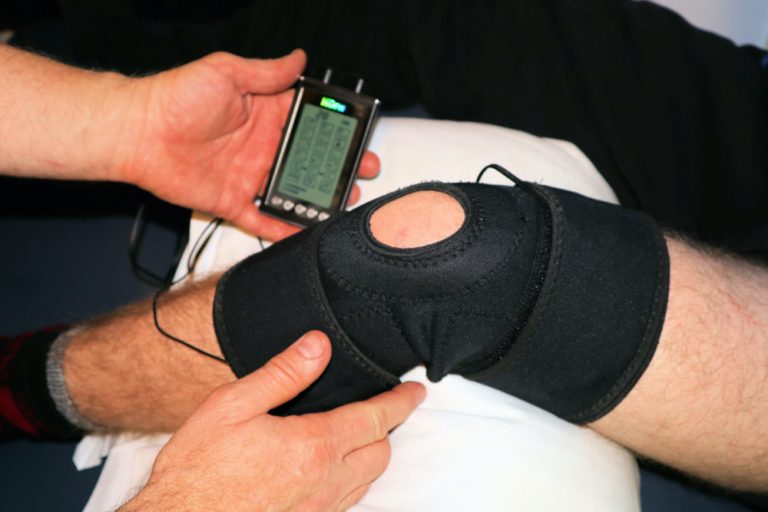 man getting E-Stem by a physical therapist on his knee wearing a black knee brace