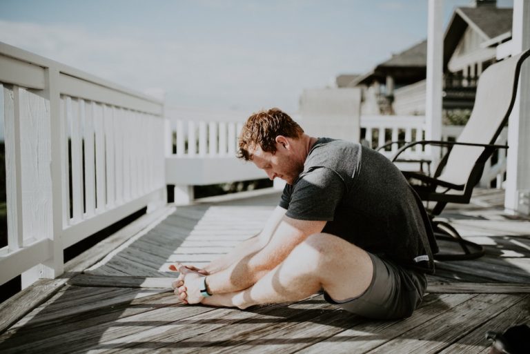 Man stretching the butterfly pose on a deck